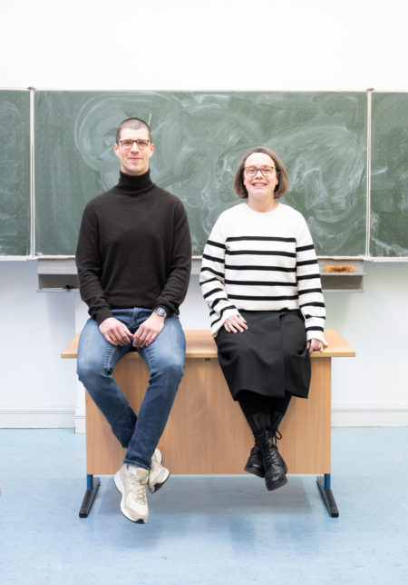 Die Lehrer Kristijan Zrinski und Hildegard Harwix sitzen auf dem Lehrerpult vor der Tafel